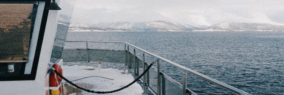Snow-covered deck of a fjord cruise boat in Tromsø, Norway, with mountain views across the water