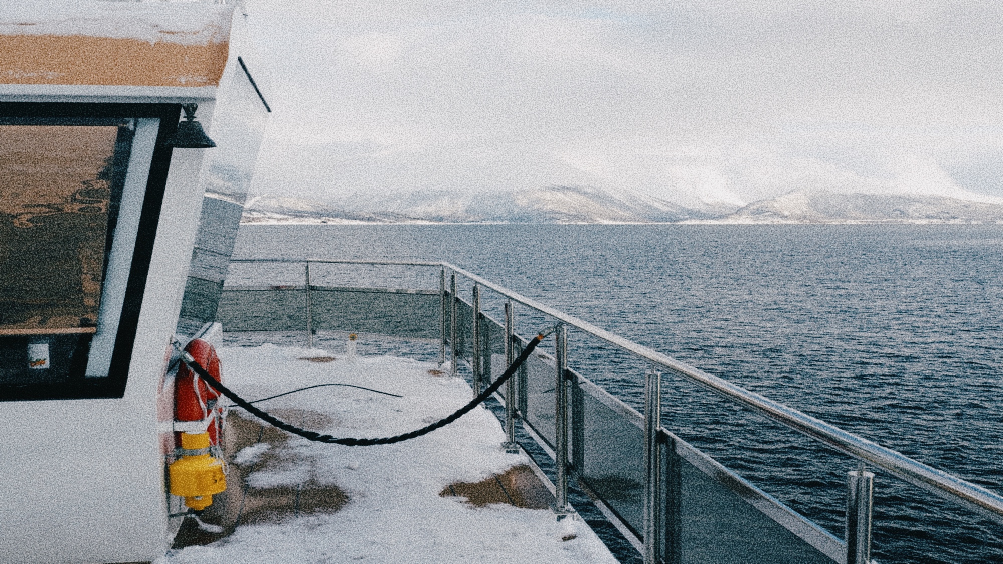 Snow-covered deck of a fjord cruise boat in Tromsø, Norway, with mountain views across the water